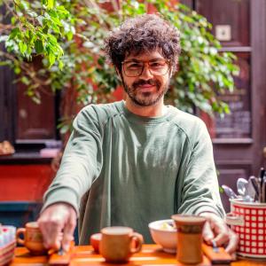 a man with glasses sitting at a table with cups at KACLLA, The Healing Dog Hostel in Lima