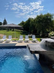 una piscina con sillas blancas y sombrilla en Maison ancestrale complètement rénovée 4 chambres, en Bromont