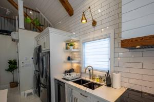 a white kitchen with a sink and a refrigerator at Kingsdale Designer Tiny House with Tesla Charger in Kitchener