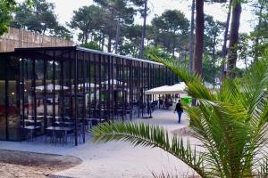 a person walking past a building with tables and chairs at VVF Lège Cap Ferret in Lège-Cap-Ferret