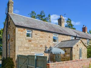 a stone house with an umbrella in front of it at Greenwood Cottage in Longframlington