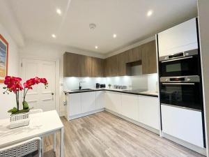 a kitchen with white cabinets and a table with red flowers at 2Bed, Private Garden & Fireplace, Near Water of Leith in Edinburgh