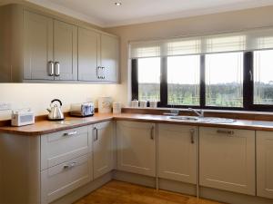 a kitchen with white cabinets and a sink and windows at Hillview in Beith