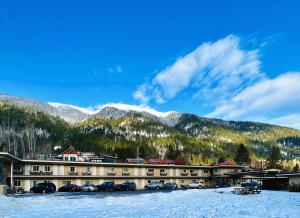 a hotel with cars parked in the snow in front of mountains at Villa Motel in Nelson