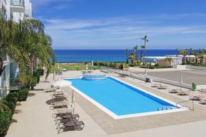 una piscina con sillas y el océano en el fondo en ALICIA - Beachfront Apartment, en Paralimni