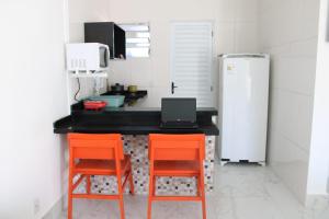 una cocina con 2 sillas naranjas y un ordenador portátil en una encimera en Kitnet Maitinga en Bertioga