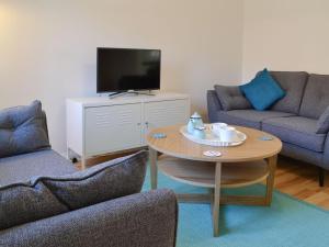 sala de estar con 2 sillas, mesa y TV en Avocet Cottage, en Sheringham