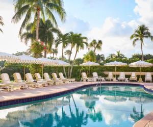 una piscina con sillas, sombrillas y palmeras en The Colony Hotel en Palm Beach