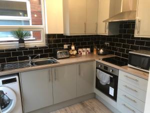 una cocina con armarios blancos y una pared de azulejos negros en Shepherds retreat, en Balby