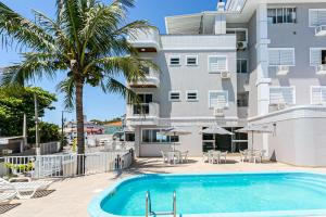 a swimming pool in front of a building with a palm tree at Prédio com apartamentos completos, com piscina e a passos da praia - Agua Marinha in Florianópolis