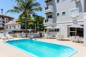 - une piscine en face d'un bâtiment avec des chaises et des parasols dans l'établissement Predio com apartamentos completos, com piscina e a passos da praia - Agua Marinha, à Florianópolis