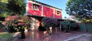 un edificio rojo con árboles y flores delante de él en Cabaña Ñangapiry en Empedrado