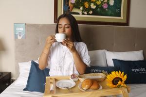 una mujer sentada en una cama bebiendo una taza de café en Hotel America Chiclayo en Chiclayo