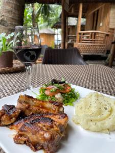 talerz żywności z mięsem i puree ziemniaczanej oraz kieliszek wina w obiekcie La Tortue Diving Resort Dauin w mieście Dauin