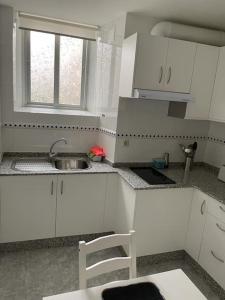 una cucina con armadi bianchi, lavandino e finestra di Acogedor piso en Cariño a Cariño