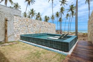 - une piscine avec un mur en pierre et des palmiers dans l'établissement Tuju Boutique Hotel, à Passo de Camarajibe