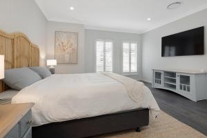 een witte slaapkamer met een groot bed en een flatscreen-tv bij 4 bedroom home with theatre room, close to CBD and beaches. in Sunshine Bay