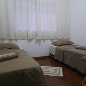 a bedroom with two beds and a window with curtains at POUSADA DO JOAO in Juiz de Fora