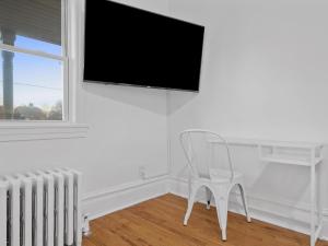 a white chair in a white room with a flat screen tv at Bloomfield/Shadyside @E Stylish and Modern Private Bedroom with Shared Bathroom in Pittsburgh