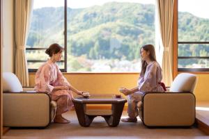dwie kobiety w kimonach siedzące w pokoju z oknem w obiekcie Hotel Hoho "A hotel overlooking the Echigo Plain and the Yahiko mountain range" formerly Hotel Oohashi Yakata-no-Yu w mieście Niigata