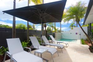 een groep stoelen en een parasol naast een zwembad bij Noosa Boutique Apartments & Elkhorn Villas in Noosa Heads
