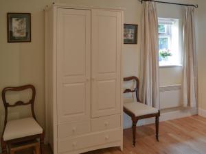 a white cabinet with two chairs and a window at Broad Cottage Boathouse in Ranworth