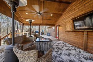 un porche cubierto con sofás, mesa y TV en Bent Tree Cabin, on Private 12.5 Acres + Hot Tub, en Broken Bow