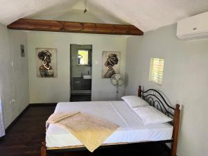 a bedroom with a bed with white sheets and a bathroom at Jamaica Colors Hotel and Eco-Retreat in Port Antonio