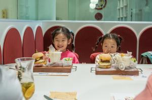 Zwei kleine Mädchen sitzen am Tisch und essen Hamburger. in der Unterkunft InterContinental Shenzhen, an IHG Hotel in Shenzhen