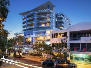 Un grand bâtiment avec des voitures garées devant lui dans l'établissement Scarborough Beach Resort Queensland, à Scarborough