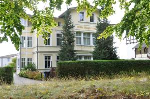 ein weißes Gebäude mit einer Hecke davor in der Unterkunft Bansin, Villa an der Waldstraße in Bansin