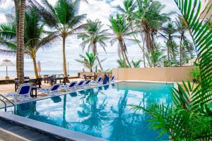 a swimming pool with chairs and palm trees at Nico Beach Hotel in Hikkaduwa