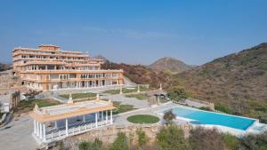 a large building with a swimming pool next to a mountain at Fateh Vilas by Fateh Collection in Udaipur