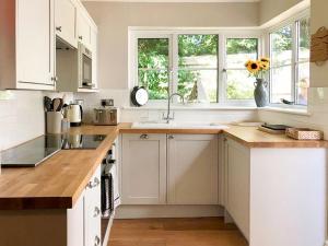 eine Küche mit weißen Schränken, einem Waschbecken und Fenstern in der Unterkunft Spring Cottage in Parkgate