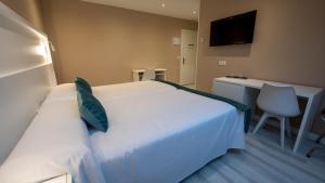 um quarto com uma cama branca, uma secretária e uma televisão em Hotel El Parador em Soto del Barco