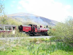 a red train is traveling down the tracks at Gwyrfai Cottage in Waenfawr