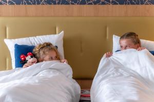 2 enfants dormant dans un lit sous les couvertures dans l'établissement Dream Castle Hotel Marne La Vallee, à Magny-le-Hongre