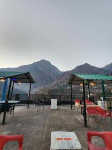 eine Terrasse mit Tischen, Stühlen und Bergen im Hintergrund in der Unterkunft Woodzo Kasol in Jari