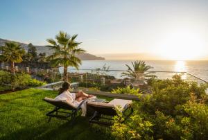 a woman sitting on a bench looking at the ocean at Les Suites at The Cliff Bay - PortoBay in Funchal