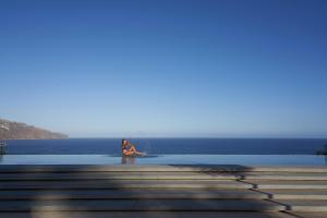 two people sitting on a dock in the water at Les Suites at The Cliff Bay - PortoBay in Funchal