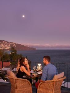 a man and woman sitting at a table on a balcony at Les Suites at The Cliff Bay - PortoBay in Funchal