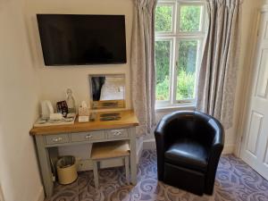 a desk with a chair and a television on a wall at Landing Cottage Guest House in Newby Bridge