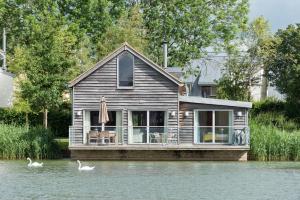 a house on a river with swans in the water at Lakeside property with hot tub Barn Owl HM08 in Somerford Keynes
