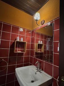 Baño de azulejos rojos con lavabo y espejo en Hostal meson del rey, en Olocau del Rey
