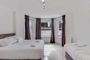 a white bedroom with two beds and a window at Hamilton Apartments hosted by Maysa London in London
