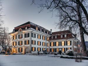 Un grand bâtiment blanc avec de la neige au sol dans l'établissement Hotel Schloss Hünigen, à Konolfingen