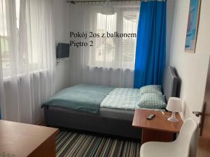 Dormitorio pequeño con cama con cortinas azules y mesa en Krysia - tuż przy plaży, en Mielno