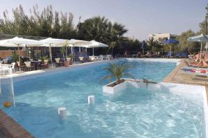 a large swimming pool in a resort with tables and umbrellas at Proimos Apartments in Gerani