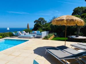 patio z krzesłami, parasolem i basenem w obiekcie VILLA JUCANOS - Vue mer panoramique Golfe de St-Tropez w mieście Cavalaire-sur-Mer
