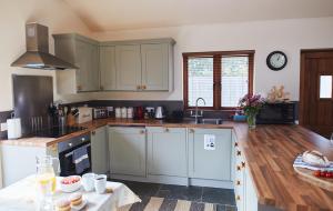 a kitchen with white cabinets and a wooden floor at The Old Dairy - Boutique Countryside Cottage at Harrys Cottages in Pen y Clawdd